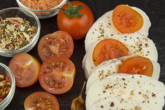 Fresh mozzarella cheese on slate board. Healthy diet meals. Preparing food for guests. Traditional meal. Mozzarella and tomatoes. Dark grey background.
