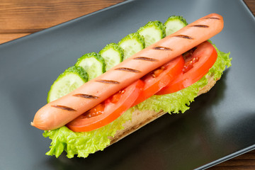 Spicy hotdog with fresh vegetables lying on black rectangular plate