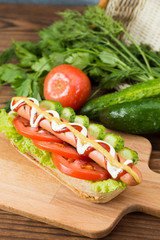 Spicy hotdog with fresh vegetables lying on wooden kitchen board