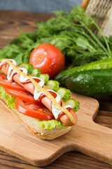 Spicy hotdog with fresh vegetables lying on wooden kitchen board