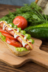 Spicy hotdog with fresh vegetables lying on wooden kitchen board
