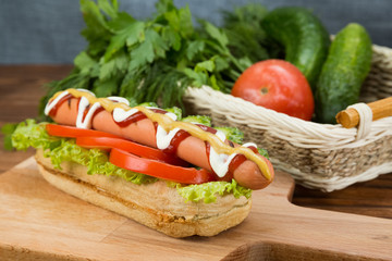 Spicy hotdog with fresh vegetables lying on wooden kitchen board