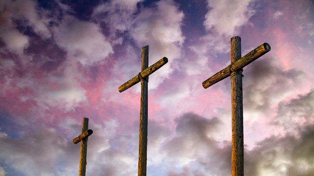 Three old rugged wooden crosses stand tall agaisnt an amazing and dramatic sunset sky.