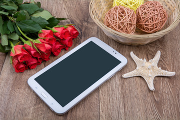 Mobile phone, white starfish and roses on a wooden background