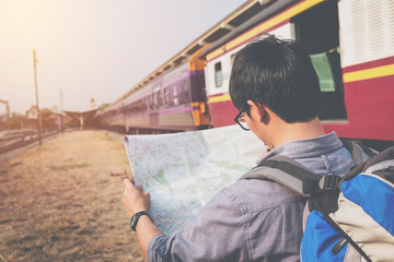 Traveler wearing backpack holding map on railway at train statio