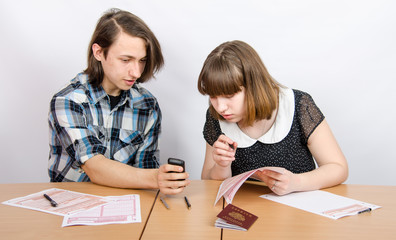 Подростки за столом с бланками подсматривают в телефон на экзамене 