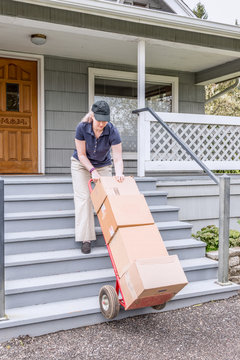 Female delivery person carrying boxes and delivering to house