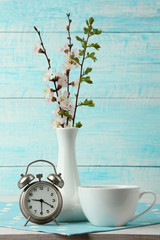 apricot branches in a vase with a Cup of coffee with the wind-up alarm clock on fabric on wooden background