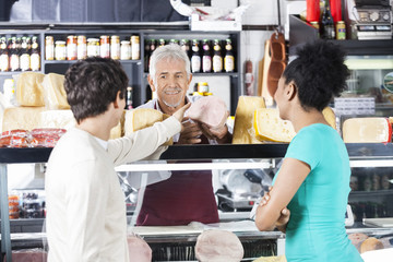 Salesman Selling Meat Piece To Couple In Grocery Store