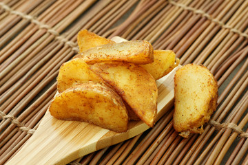Fried potato wedges on wooden spatula. Close up.