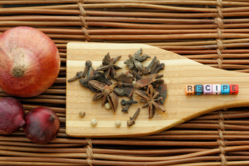 Clove,coriander,star anise and alphabet block forming a word RECIPE on wooden spatula with small and big onion