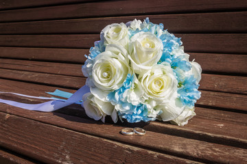 artificial bouquet of white roses and wedding rings are on the b
