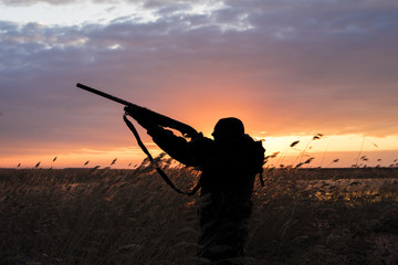 Silhouette du chasseur avec le fusil de chasse sur un fond de coucher de soleil