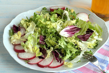 Radishes and fresh lettuce.  Radishes and fresh lettuce on a white dish on a blue wooden background.