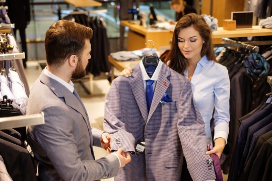 Confident handsome man with beard choosing a jacket in a suit shop.