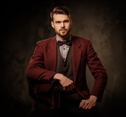 Young handsome old-fashioned man with briefcase posing on dark background.