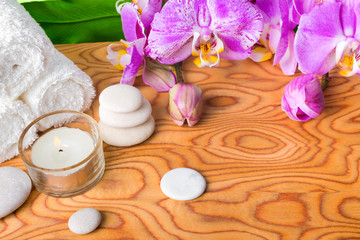 Obraz na płótnie Canvas beautiful spa setting with blooming lilac orchid, white stones, towels, candle and big green leaf on root wood background, close up