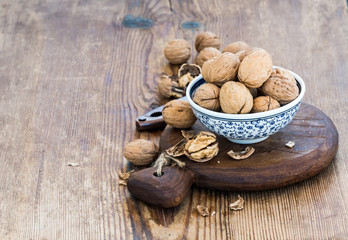 Fototapeta na wymiar Walnuts in ceramic bowl and on cutting board with nutcracker over rustic wooden background