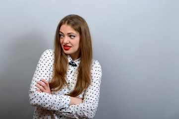 Girl with condemning glance, crossed hands on grey background