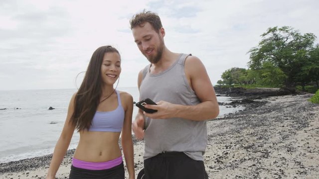 Runners taking selfie after running workout run. Good looking young man and woman taking a self-portrait photo with smart phone camera after exercising on a beach. Mixed race couple. RED EPIC.