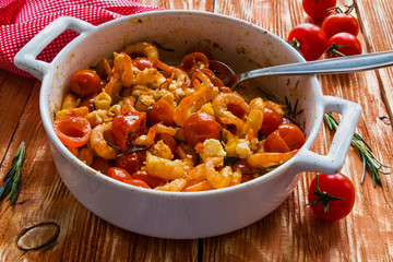Shrimps in white baking dish on wooden background. Baked with cherry tomatoes and feta cheese.
