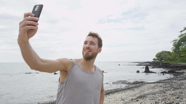 Sporty man taking selfie photo using phone after running and fitness workout outside on beach. Good looking athlete finishing exercise with smartphone self portrait. RED EPIC SLOW MOTION.