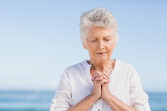 Senior woman praying on the beach - Powered by Adobe