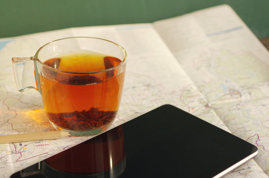 Cup of tea, the black tablet, card, the tourist map. Preparation of a route of travel.