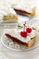 Slice of homemade pie with cherry and meringue decorated cherry blossom on white wooden desk