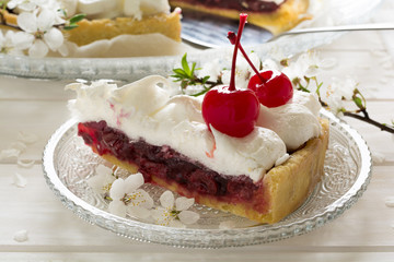 Slice of homemade pie with cherry and meringue decorated cherry blossom on white wooden desk