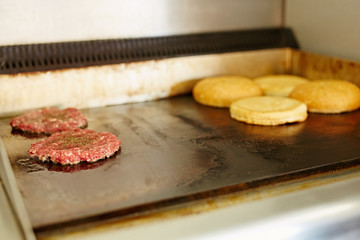 Burger patties frying on a grill with open buns toasting