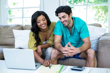 Happy couple with laptop discussing on bills