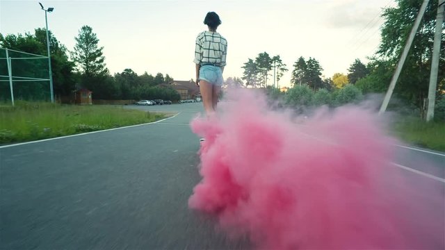 Woman on skateboard with a trail of pink smoke