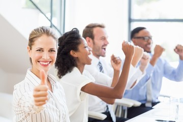 Businesswoman showing her thumbs up in office while team celebrating in background