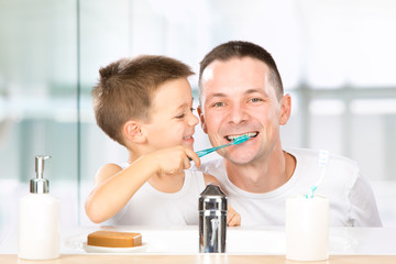 smiling child brushes his teeth with dad in the bathroom