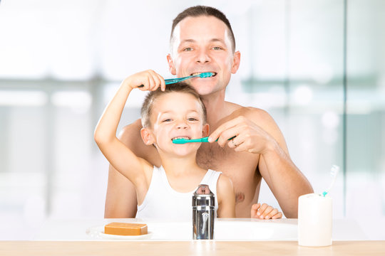smiling child brushes his teeth with dad in the bathroom