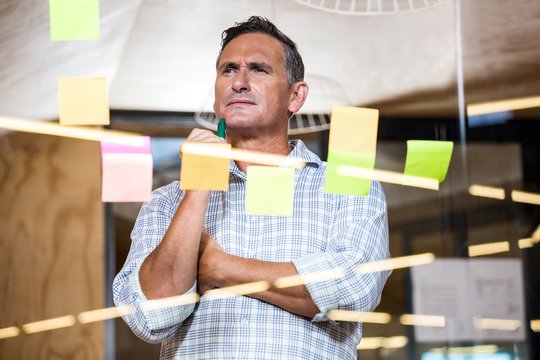 Thoughtful man looking at sticky notes on window