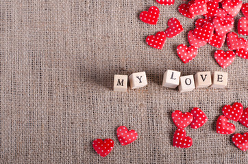 Words My love on wooden cubes and many red decorative hearts on sackcloth, canvas background. Vintage style.
