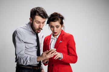 Business concept. The two young colleagues holding mobile phone on gray background
