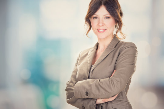 brunette young businesswoman smiling with arms folded at office