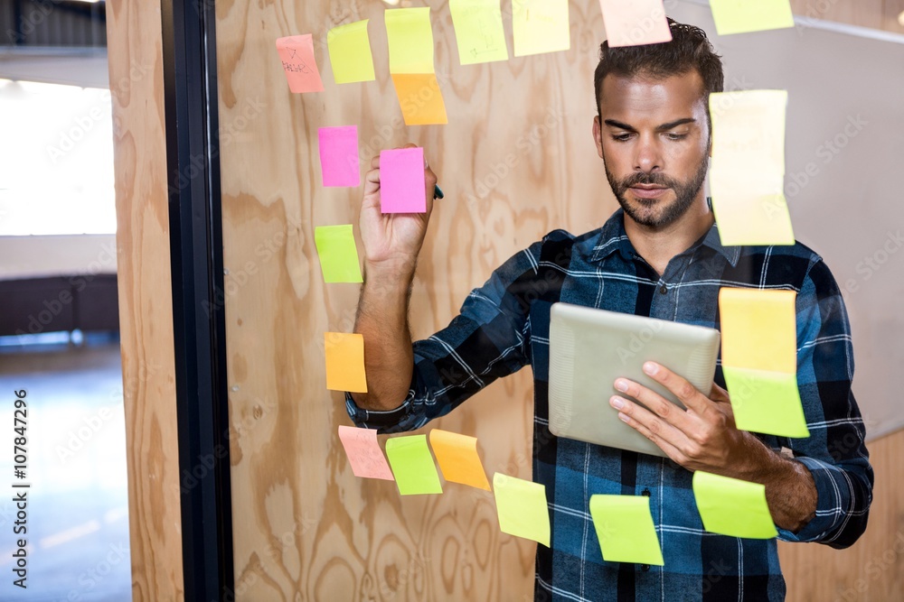 Aufkleber Man using digital tablet while writing on sticky notes 