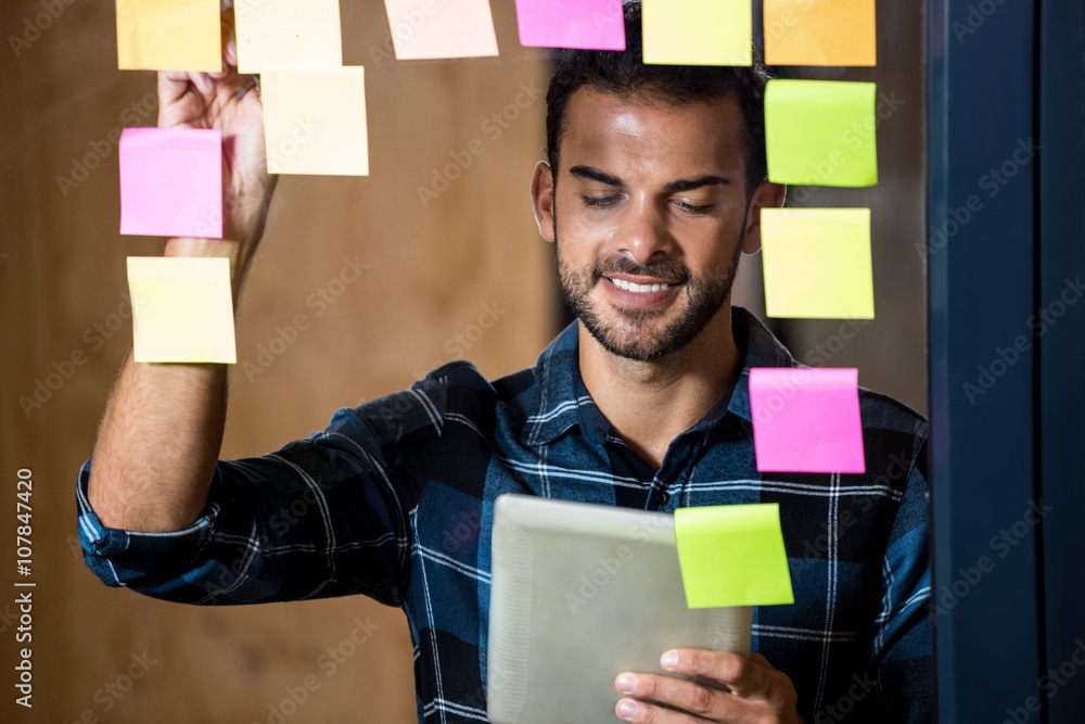 Aufkleber Man using digital tablet while writing on sticky notes 