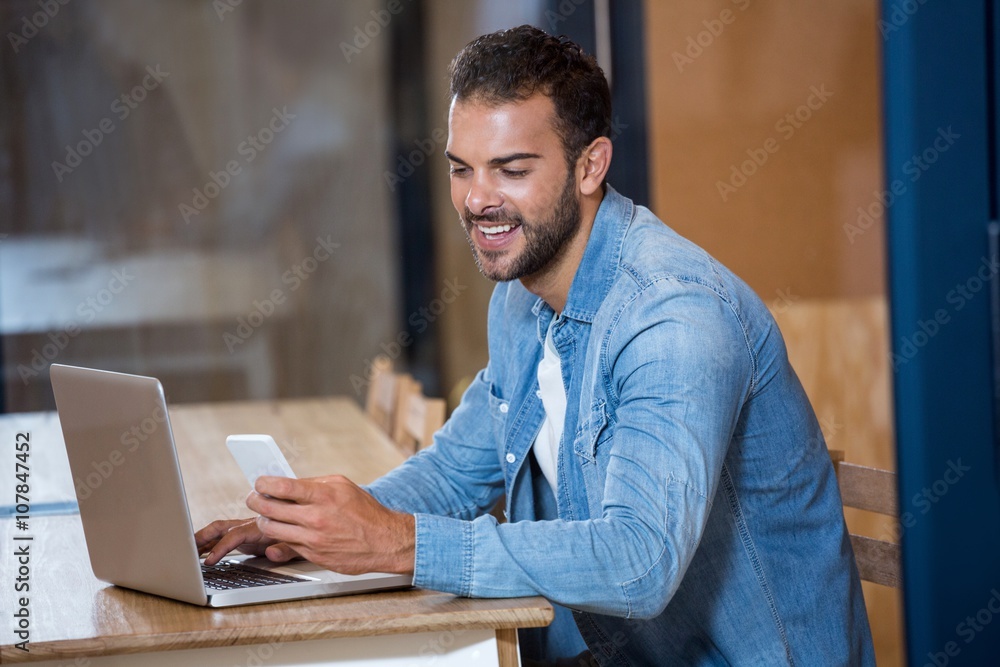 Aufkleber Man text messaging on phone while sitting on desk with laptop