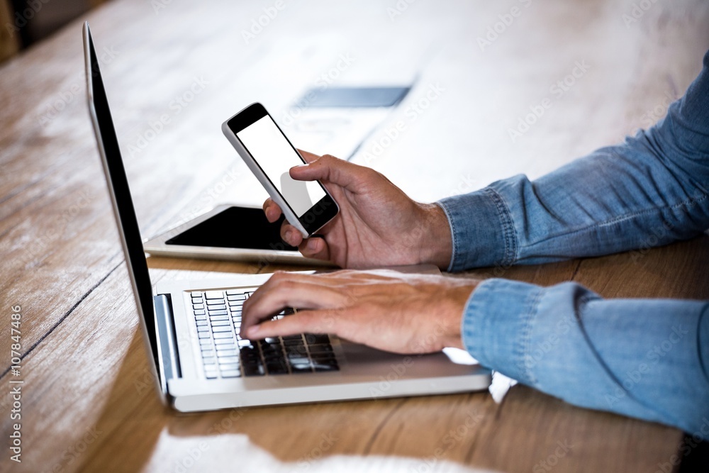 Aufkleber Man text messaging on phone while using a laptop