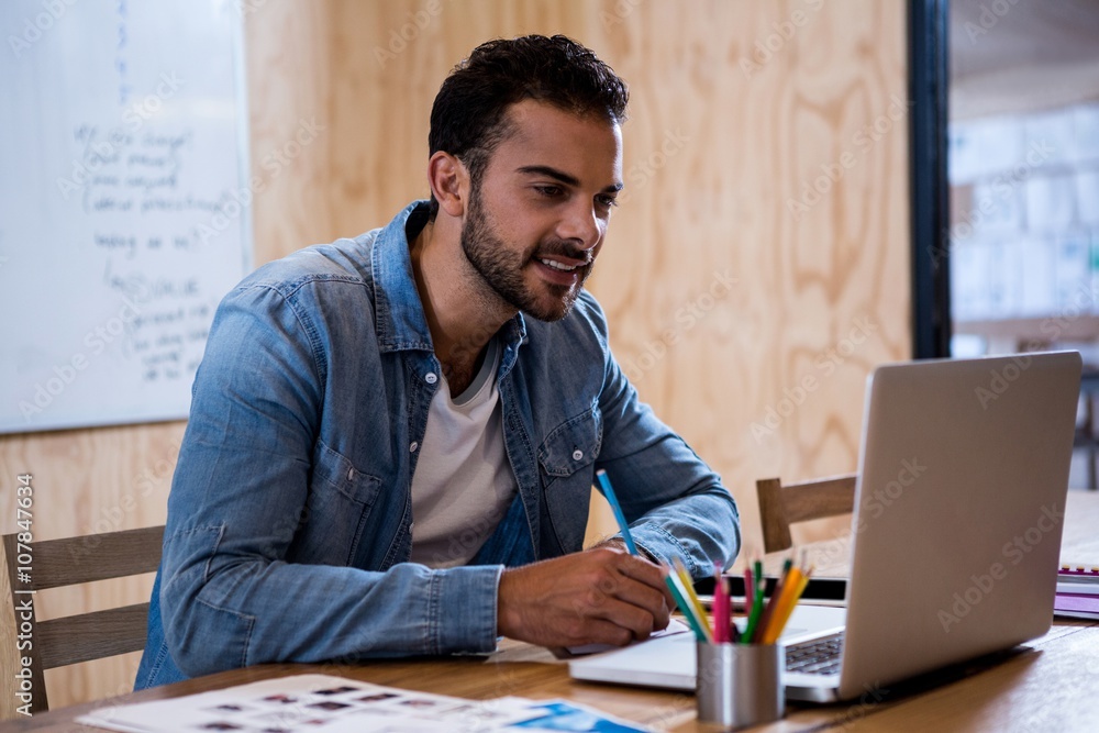 Aufkleber Man writing note on diary while using laptop