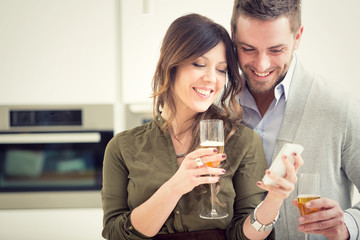 young casual couple cheers with champagne and phone in the kitchen