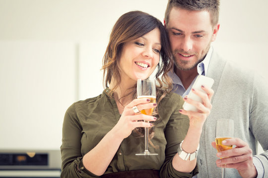 young casual couple cheers with champagne and phone in the kitchen