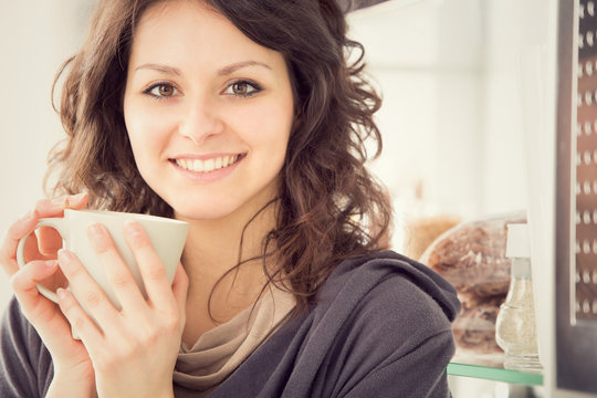 young smiling woman with cup of tea in the kitchen