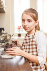 Young teenage girl sieving flour through the sieve