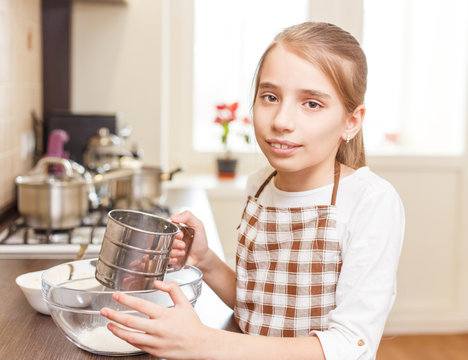 Small girl in apron holding sieve preparing flour
